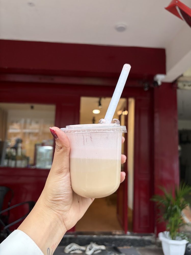 Pink layered strawberry latte held up outside the café